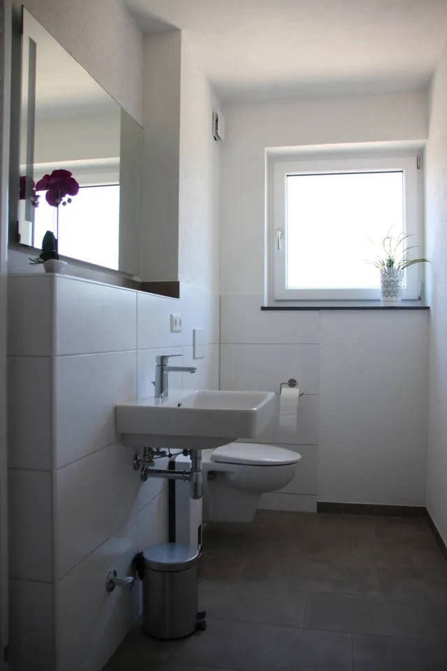 Blick ins Badezimmer mit Waschbecken, Toilette und Tageslichtfenster.