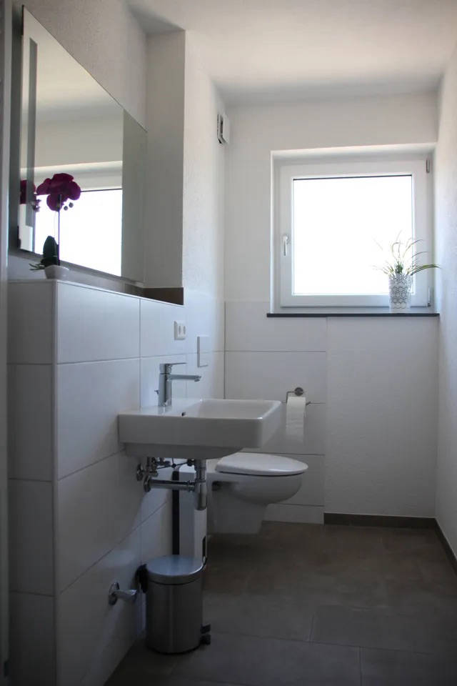 Blick ins Badezimmer mit Waschbecken, Toilette und Tageslichtfenster.