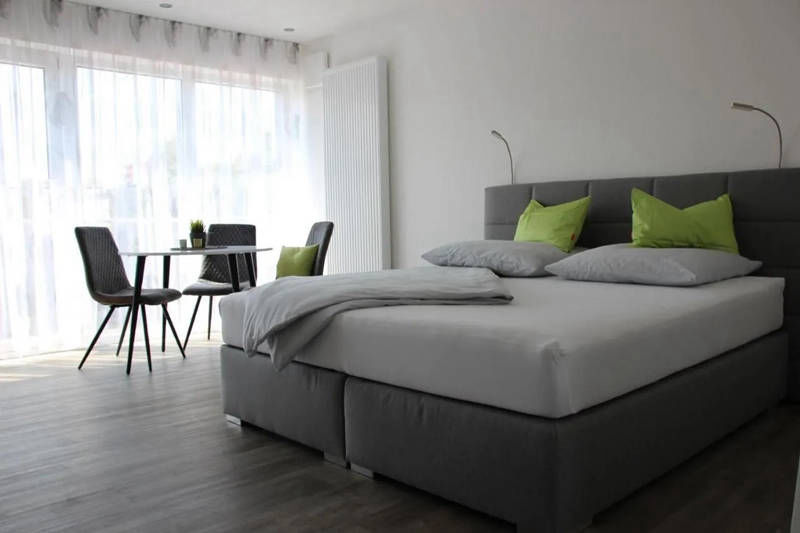 Blick Richtung Fensterfront mit Tisch und Bett.