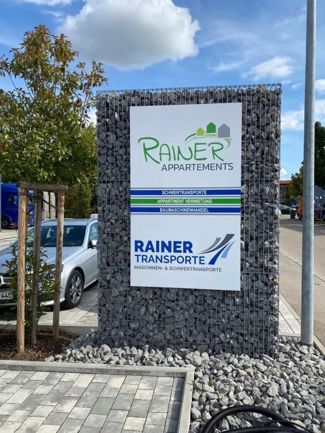 Begrüssungsschild am Parkplatz mit Hinweis auf Rainer Appartements und Rainer Transporte.
